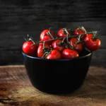 schwarze schale mit roten tomaten auf holzbrett von food fotograf hannover, dem fotograf in der nähe.