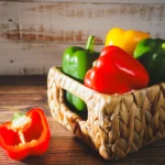 geflochtener weidenkorb gefüllt mit bunten paprika auf holztisch von food fotograf hannover dem fotograf in der nähe.