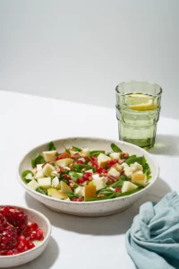 Obstsalat mit Nüssen, ausgewogene Ernährung, sauberes Essen. Spinat mit Äpfeln, Pekannüssen und Feta, garniert mit Granatapfelkernen in einer Schüssel auf einem Tisch mit weißer Tischdecke. Hartes Licht, Schatten, vertikal von food fotograf hannover.