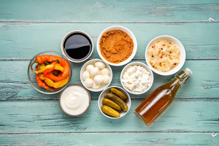 Verschiedene fermentierte Lebensmittel, darunter Gurken, Sauerkraut, Sojasauce, Miso, Milchprodukte und Apfelessig auf helltürkisem Hintergrund. Gesundes Ernährungskonzept für Immunität und Darm von food fotograf hannover.