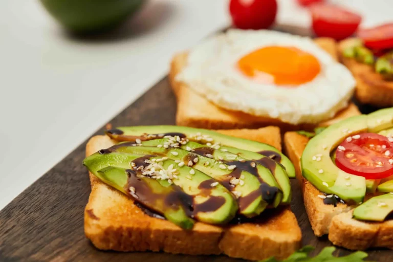Nahaufnahme eines Frühstückstellers mit Toastscheiben, belegt mit Avocadoscheiben, einem Schuss Balsamico-Glasur, Sesamkörnern, Tomatenscheiben und einem Spiegelei bei food fotografie hannover