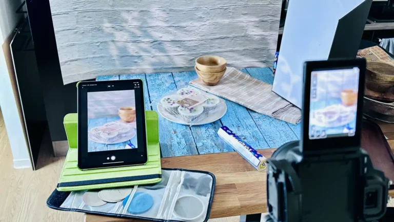 Eine auf einem Stativ montierte Digitalkamera ist auf die Aufnahme eines auf ihrem Bildschirm angezeigten Food-Fotografie-Setups fokussiert, mit einem unscharfen Fotohintergrund, der eine Küchentheke und einen weiteren Bildschirm zeigt im Fotostudio Hannover von Food Fotograf Hannover Stephan Eckert.